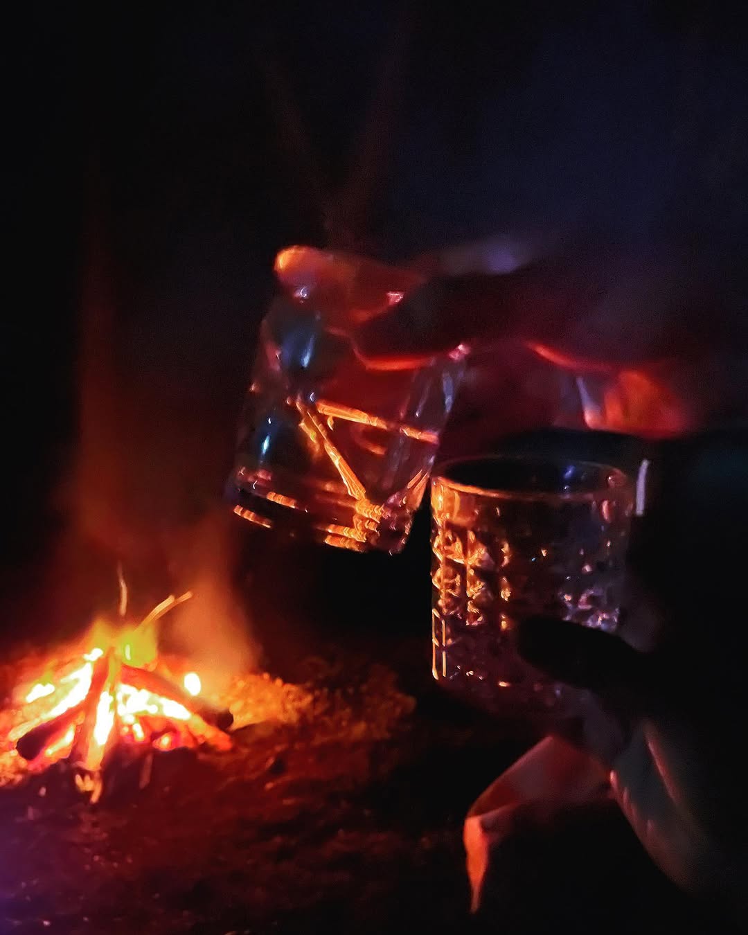 Two glasses toasted near the campfire with orange flames glowing in the dark