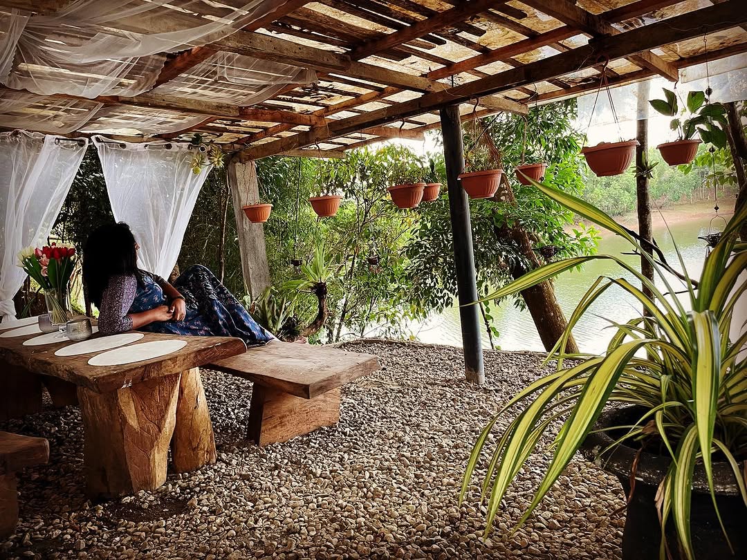 Pavilion lounge area — rustic pergola with hanging plants and lake view, person relaxing on bench